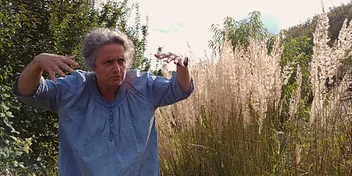 Anne en plein air, bras tendus en geste expressif, devant des roseaux