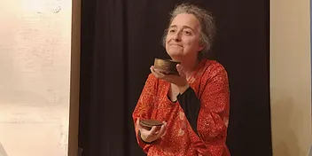 Anne en spectacle, deux petits bols de bois entre les mains, expression complice