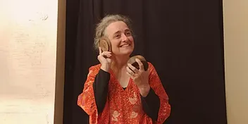 Anne en spectacle, elle approche une noix de coco sculptée de son oreille en souriant